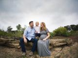 Dad and expectant mom with toddler sitting on rocky outcrop