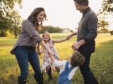Couple twirling their children in a grassy field